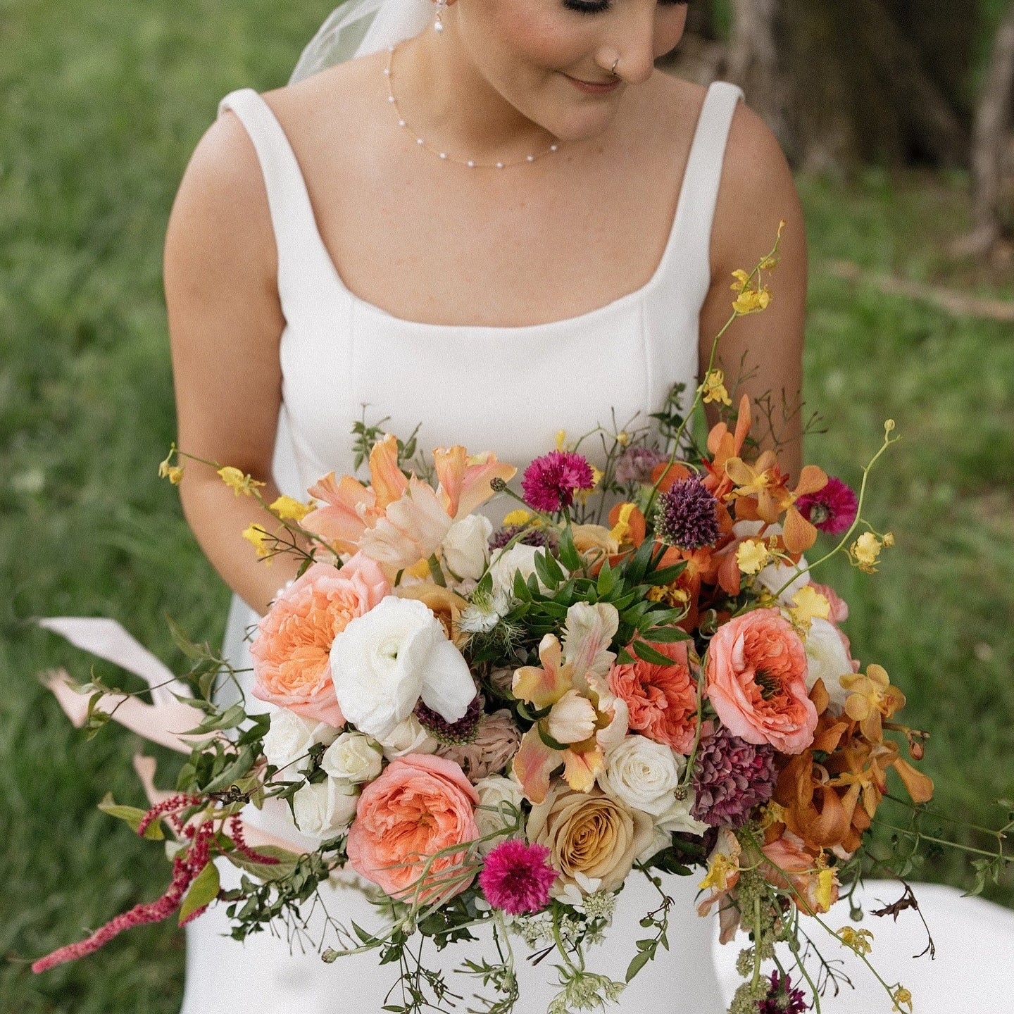 Woman in a white dress holding a colorful bouquet of flowers in a natural setting.