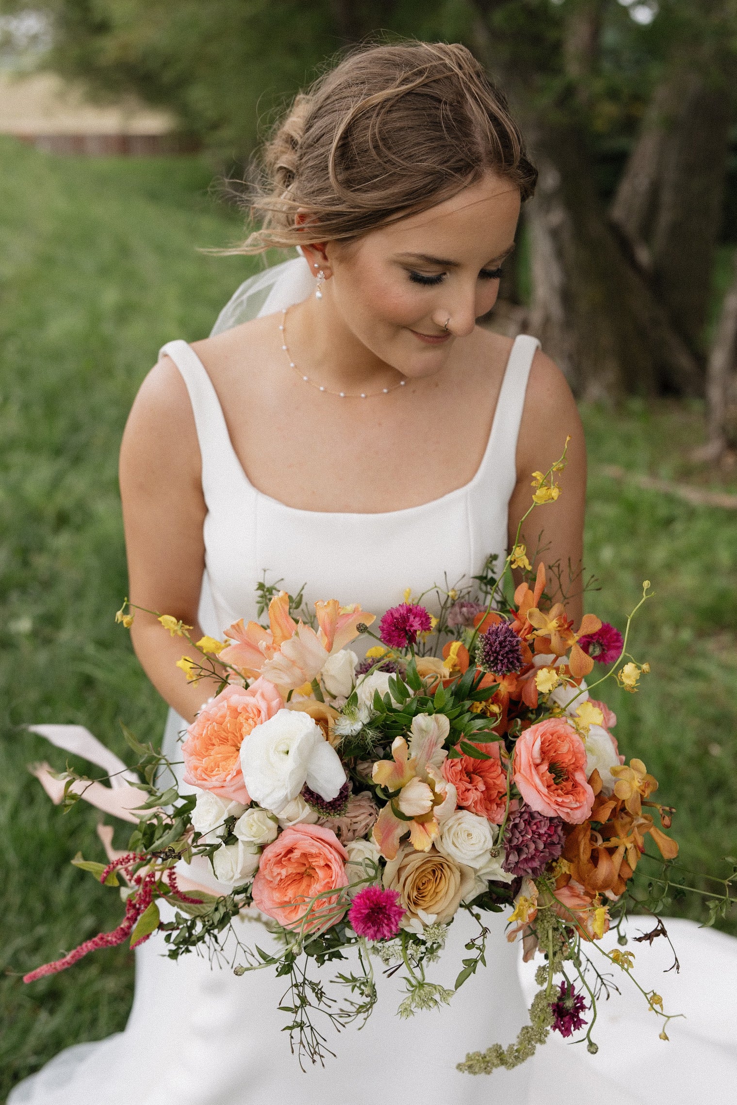 Woman in a white dress holding a colorful bouquet of flowers outdoors.
