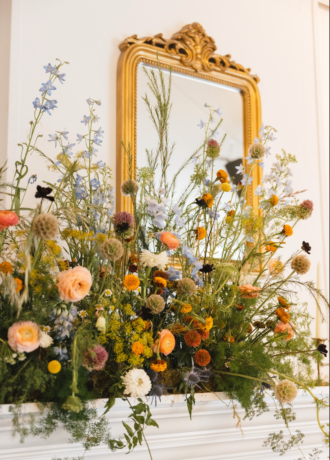 Decorative mirror with gold frame above a floral arrangement on a white surface.