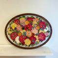 Load image into Gallery viewer, Oval frame with pressed flowers in a wooden frame on a white surface.