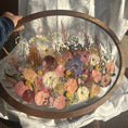 Load image into Gallery viewer, Oval frame with pressed flowers held by a person on a white background