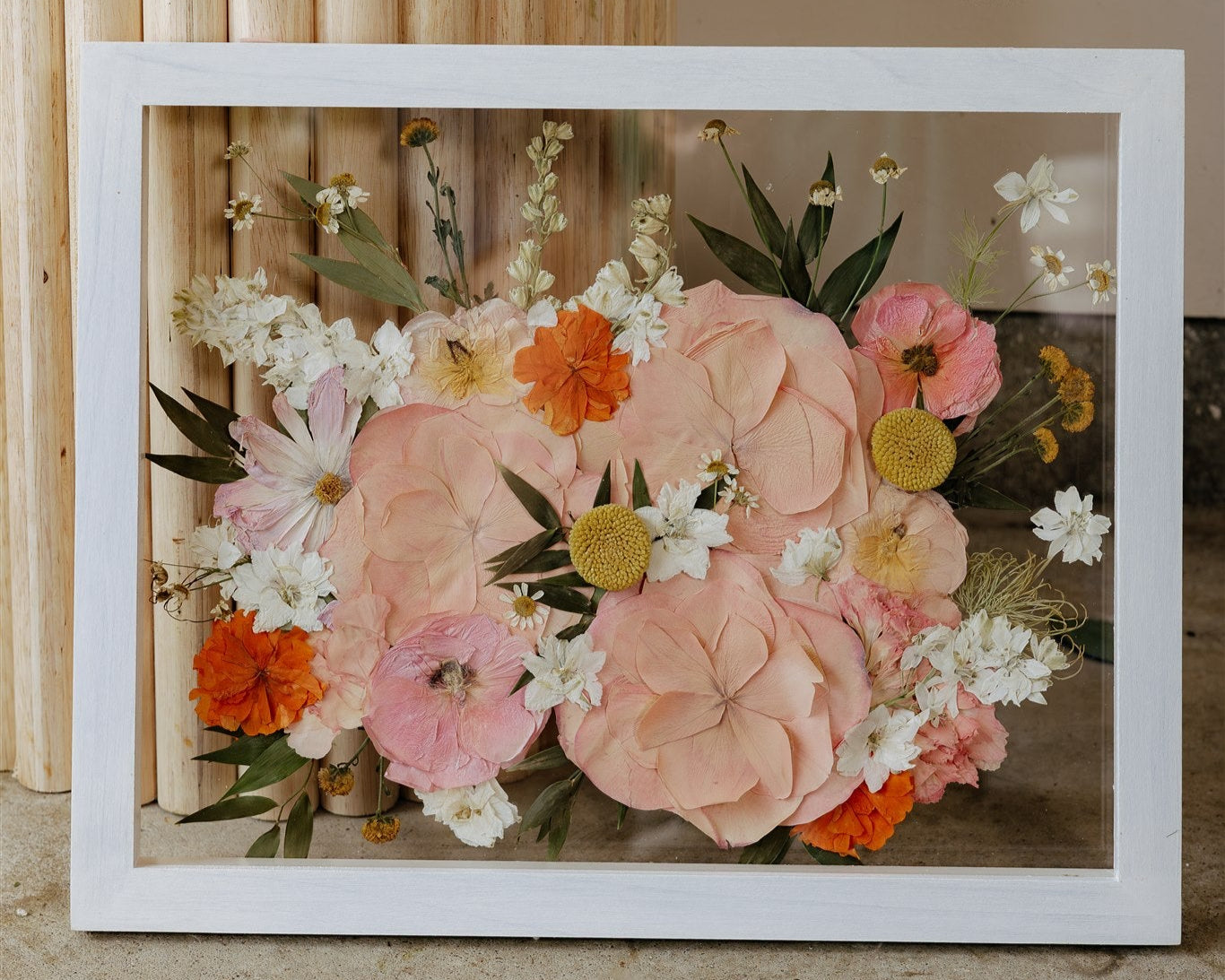 Framed arrangement of pink, orange, and white flowers on a wooden surface.