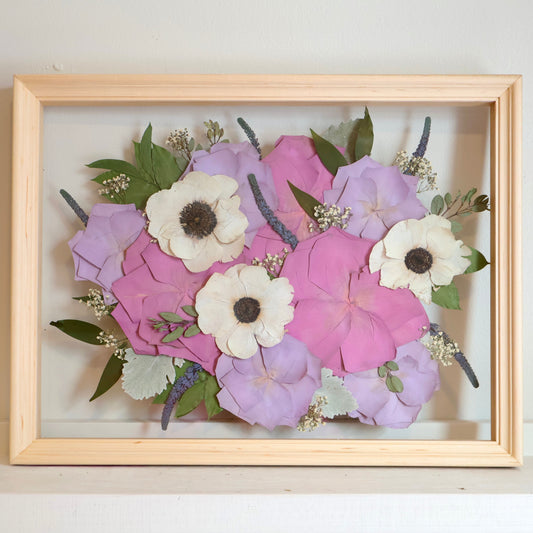 Framed arrangement of purple and white flowers on a light background