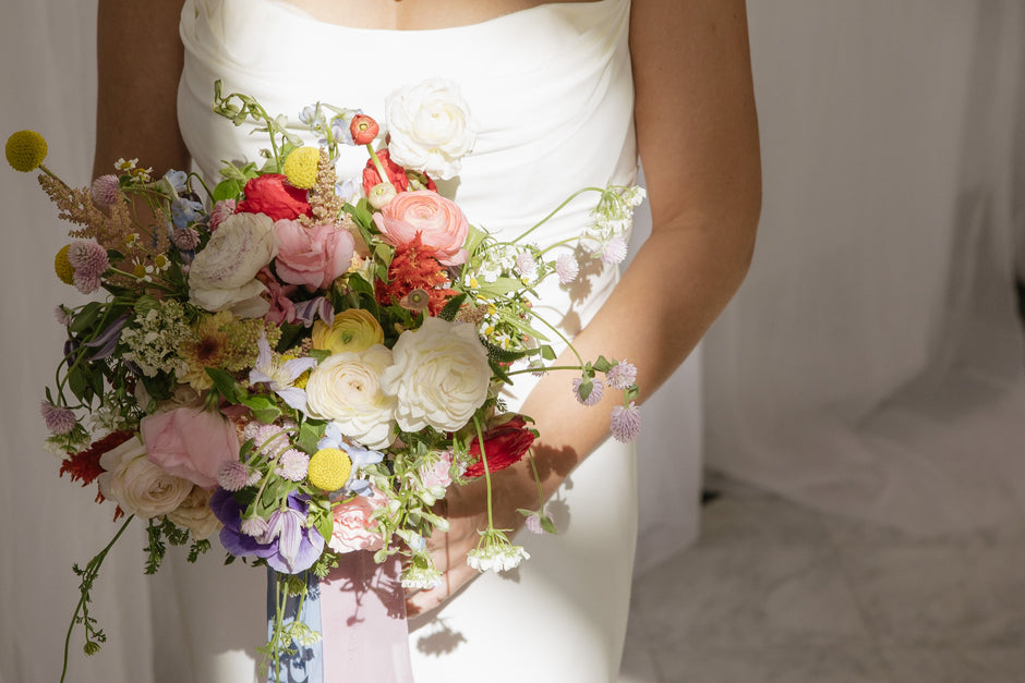 Woman in a white strapless dress holding a colorful bouquet against a white background