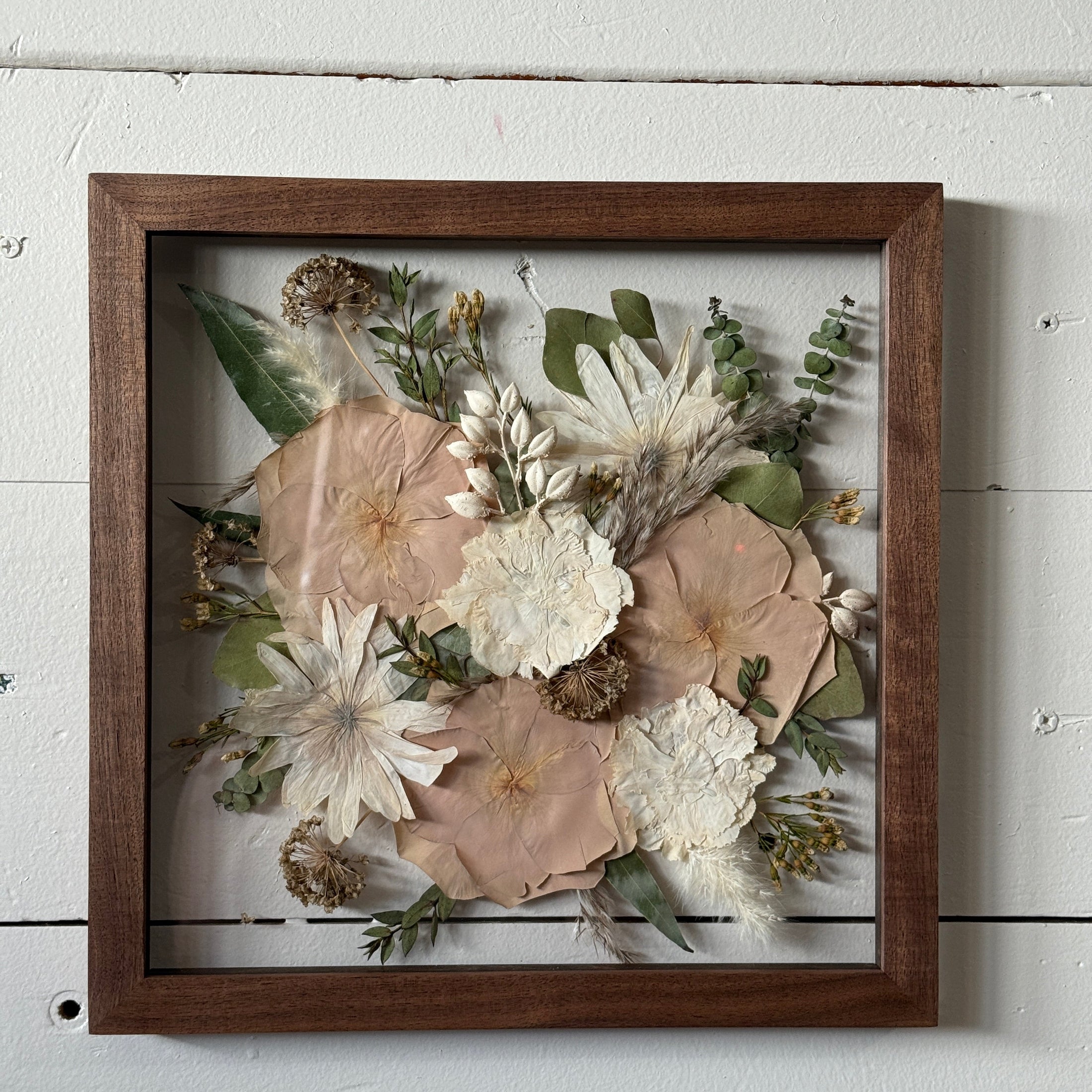 Framed arrangement of pressed flowers on a white wooden surface