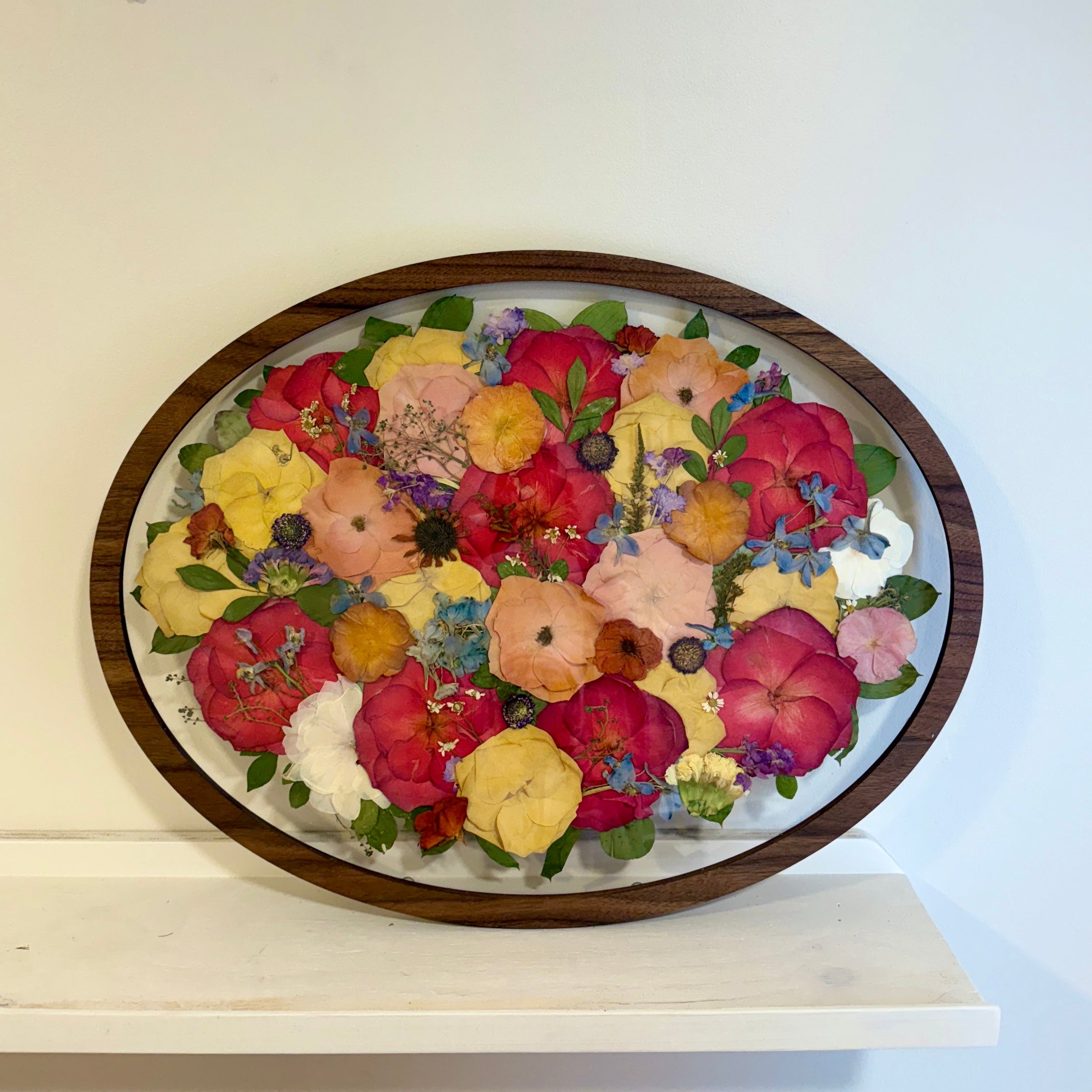 Oval frame with pressed flowers in a wooden frame on a white surface.