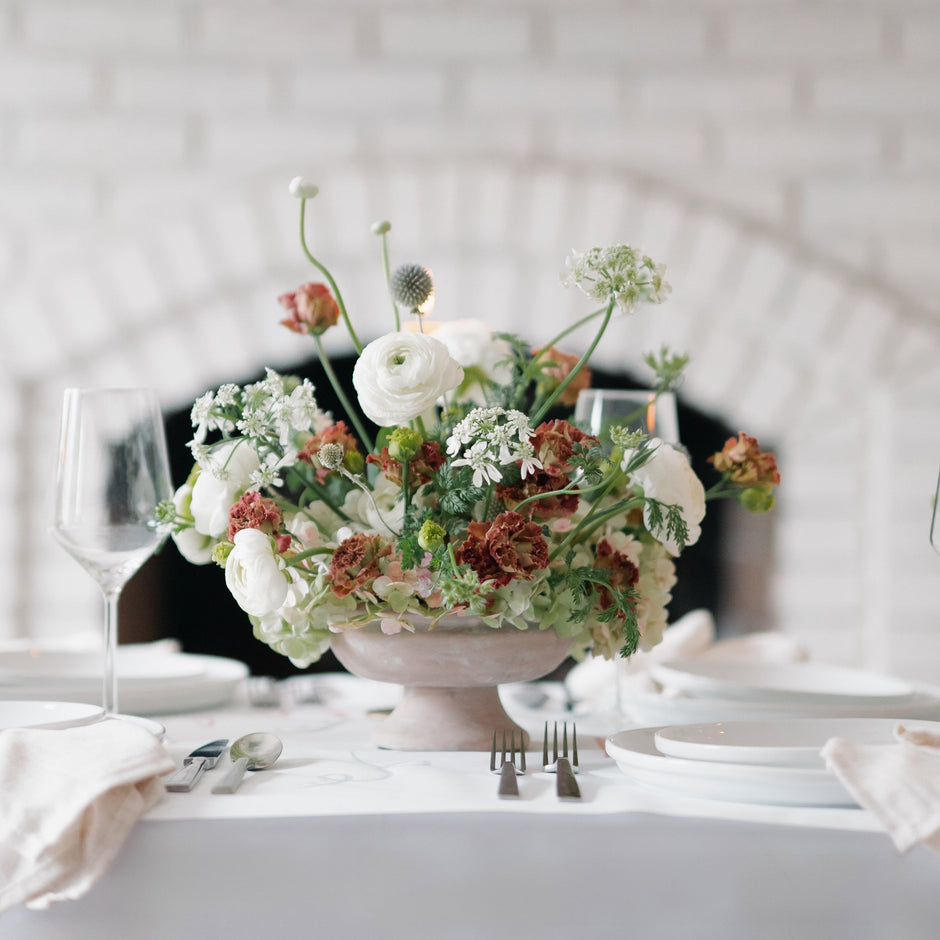 Table setting with floral centerpieces against a white brick wall.