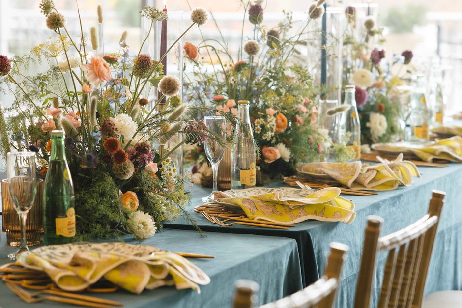 Elegant table setting with floral arrangements and green tablecloth in a bright room.