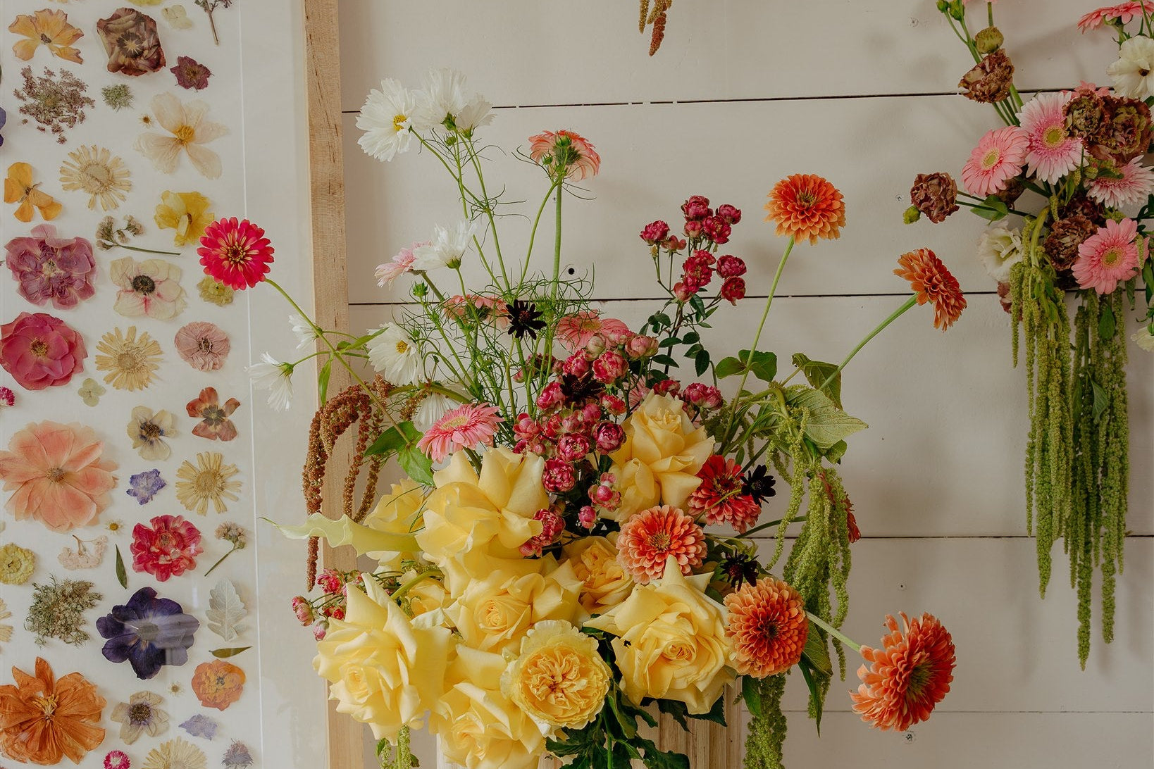 Floral arrangements and a framed floral collage on a wooden wall.