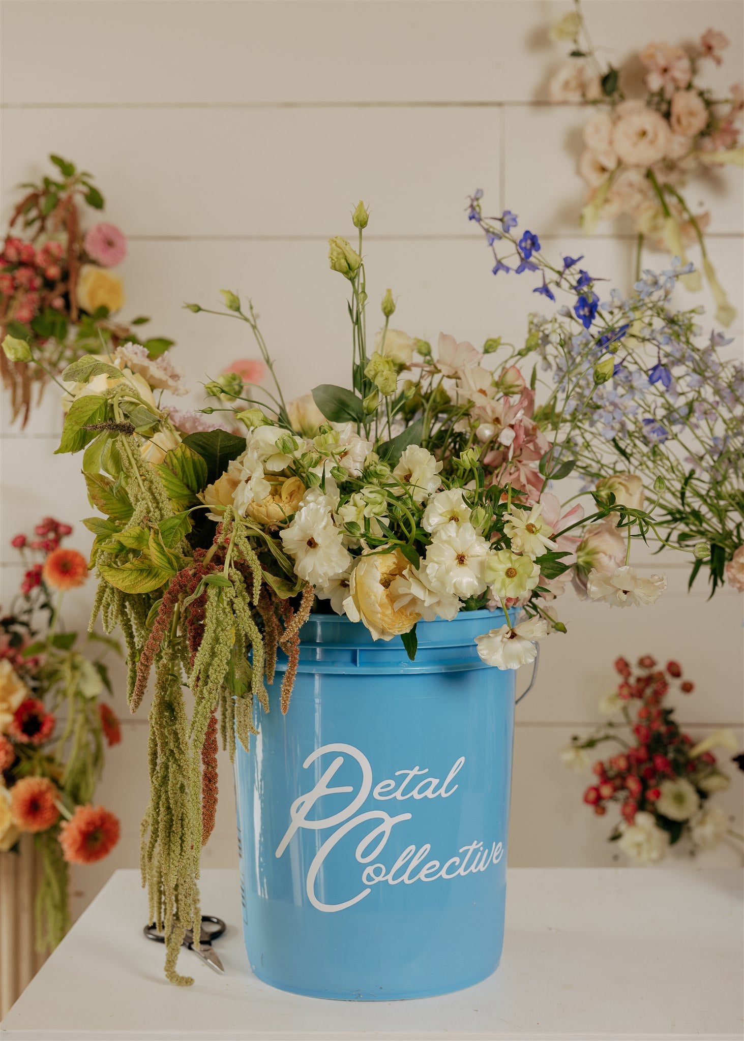 Blue bucket filled with flowers labeled 'Petal Collective' against a white background