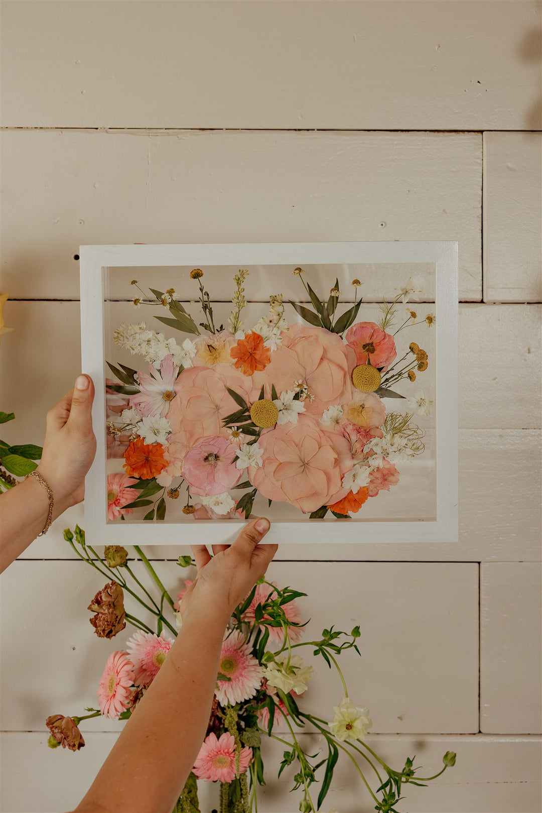 Person holding a flower preservation frame against a wooden wall